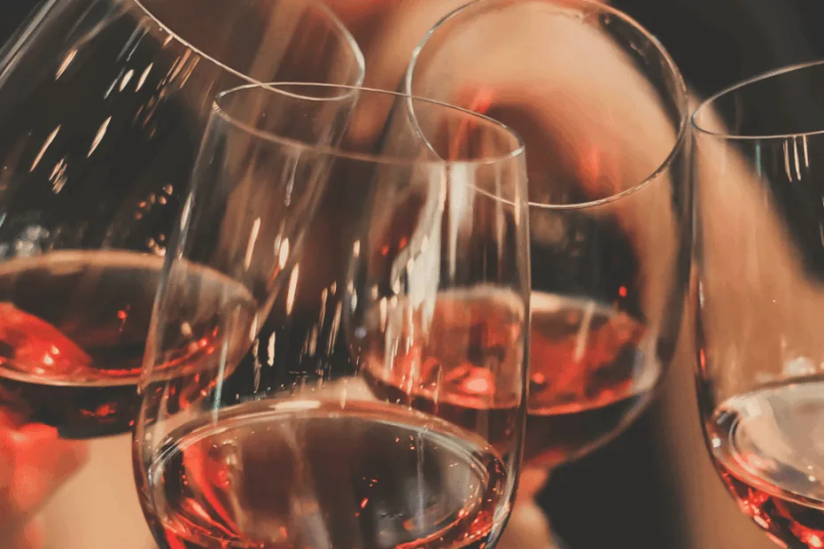 Quatro mãos brindam com taças de vinho tinto em uma celebração.