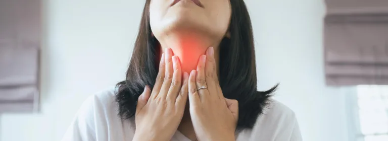 Uma mulher de camisa branca segura a garganta, destacada em vermelho, indicando dor ou desconforto.