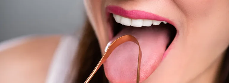 Close-up de uma pessoa usando um raspador de língua de cobre na língua estendida.
