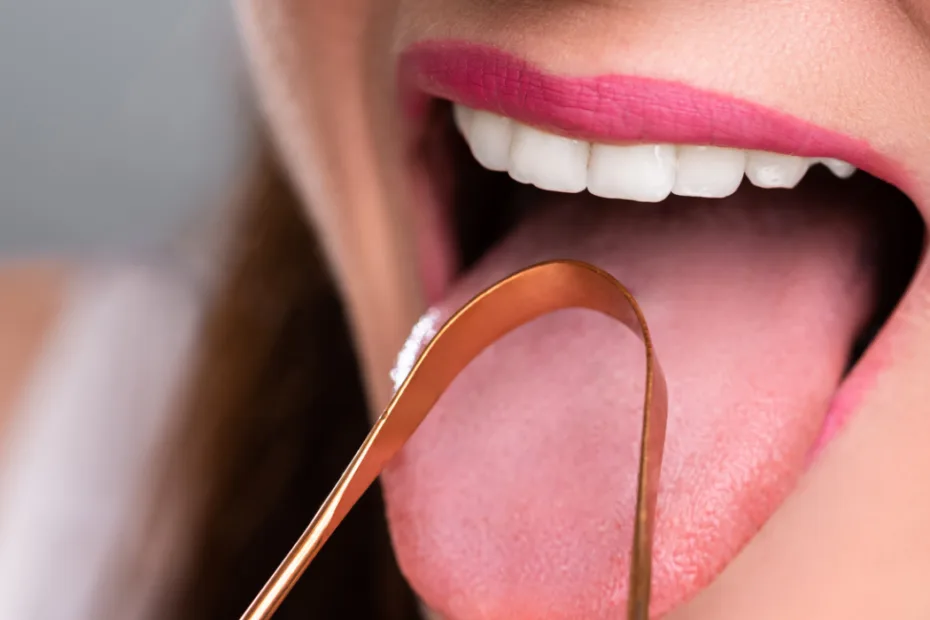 Close-up de uma pessoa usando um raspador de língua de cobre na língua estendida.