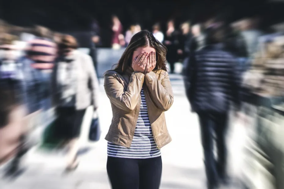 Uma mulher está de pé em uma rua movimentada e desfocada, cobrindo o rosto com as mãos, transmitindo uma sensação de ansiedade ou pânico.