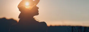 Silhueta de uma mulher de chapéu ao pôr do sol, com o sol criando um efeito de halo em sua cabeça.