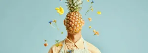 Retrato surreal de uma pessoa com um abacaxi no lugar da cabeça, vestindo um avental cor de creme, cercada por flores coloridas e com um fundo azul.
